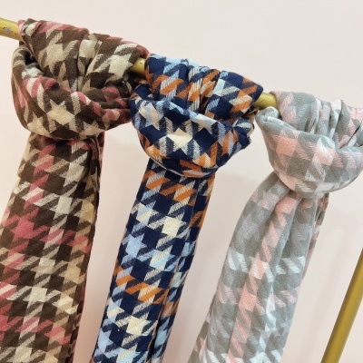 Três cachecóis com padrão pied-de-poule em castanho, azul e cinzento pendurados num varão amarelo