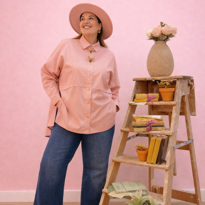 Mulher com roupa rosa e azul junto a escada de madeira com livros e vasos