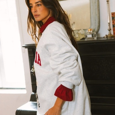 Mulher com sweatshirt cinza claro e camisa vermelha numa sala com mobília clássica escura