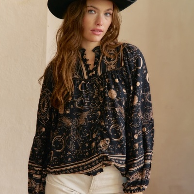 Modelo com blusa preta de padrão celestial dourado, calças claras e chapéu preto