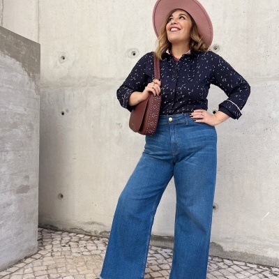 Mulher com roupa casual e chapéu rosa contra parede de cimento claro