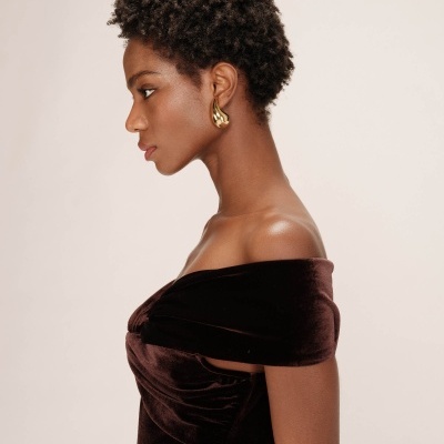 Modelo de perfil com vestido de veludo castanho e brinco dourado