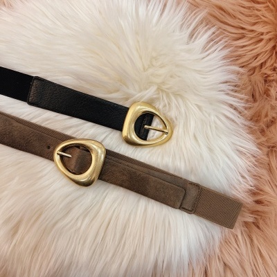 Dois cintos, preto e castanho, com fivelas douradas, sobre tapete peludo branco e rosa.