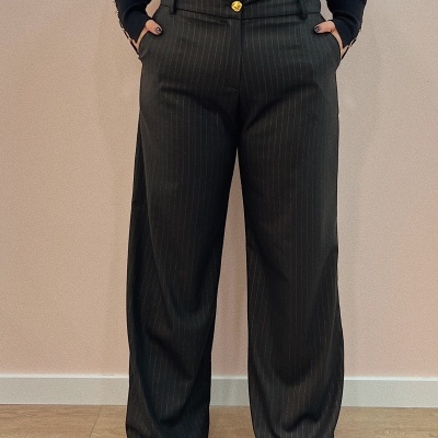 Calças compridas risca de giz castanho escuro com botão dourado, camisa preta e sapatos vermelhos.