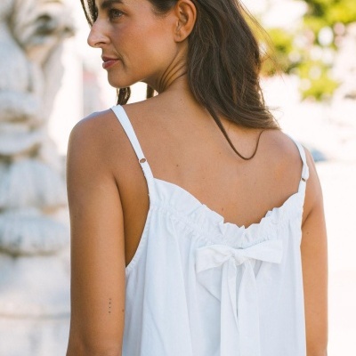 Top feminino branco com alças finas e laço nas costas, visto de costas ao ar livre