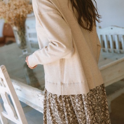 Camisola bege de malha e saia floral castanha e branca em ambiente interior