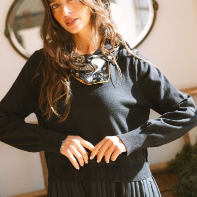 Mulher com blusa preta, saia preta plissada e lenço azul com padrão floral no pescoço