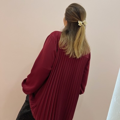 Blusa vinho plissada com calças pretas brilhantes e laço dourado no cabelo
