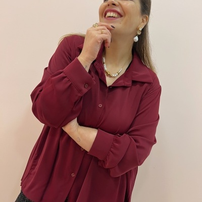 Mulher sorridente com camisa bordeaux e colar de pérolas