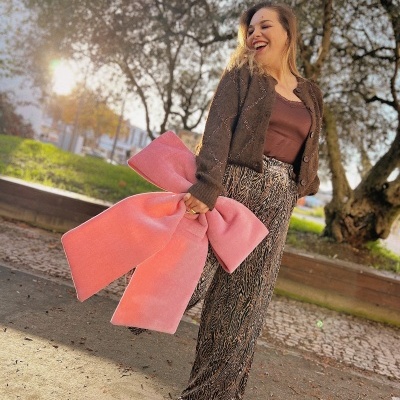 Pessoa de roupa castanha e calças com padrão animal print segurando laço rosa em ambiente exterior