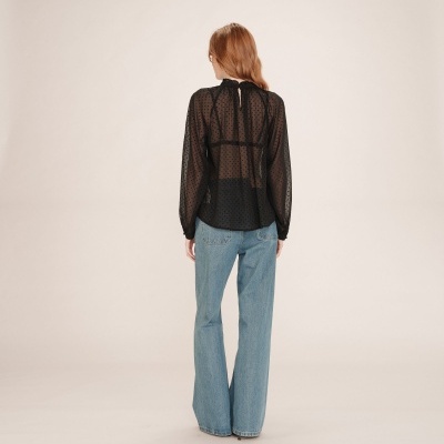 Pessoa de costas a usar blusa preta transparente de bolinhas e calças de ganga azuis