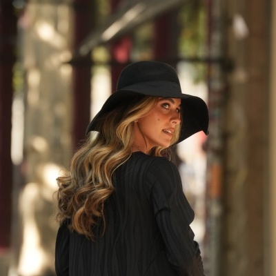 Mulher de cabelo loiro ondulado com chapéu preto e vestido preto