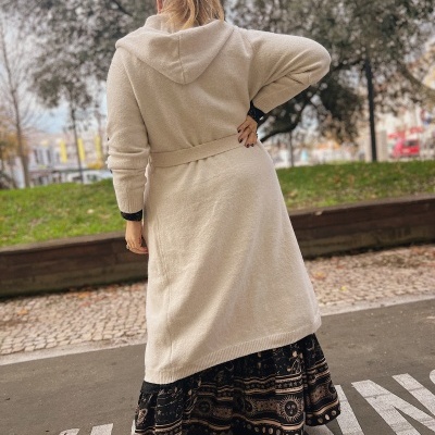 Capa longa de malha beje com capuz e cinto à cintura vista de costas em ambiente exterior