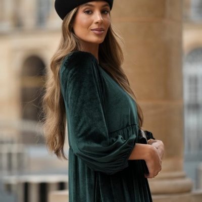 Mulher com vestido verde de veludo e boina preta em ambiente urbano