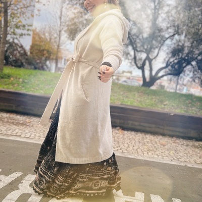 Mulher com casaco creme comprido e vestido preto com padrão celestial ao ar livre