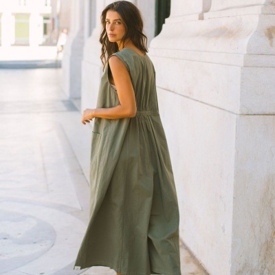 Vestido longo verde-oliva sem mangas usado por mulher em ambiente exterior urbano.