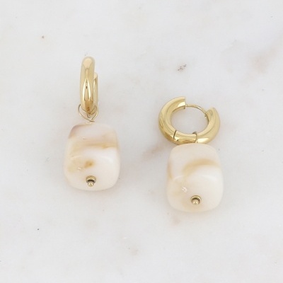 Brincos com argolas douradas e pendentes quadrados creme em superfície branca de mármore