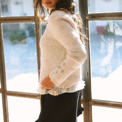 Mulher com camisola branca de malha e saia preta de malha junto a uma janela