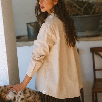 Mulher de cabelos castanhos com camisa bege e saia preta ao lado de cadeira com estofado de pêlo.