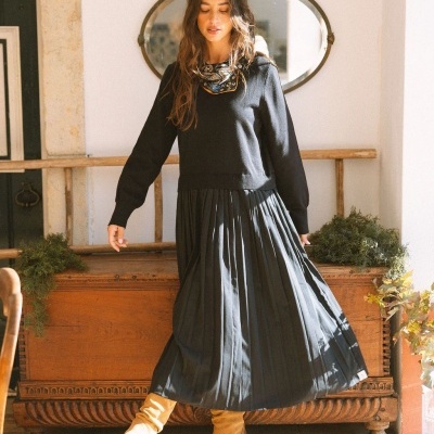 Mulher a usar vestido preto e botas amarelas com móvel rústico e espelho oval ao fundo