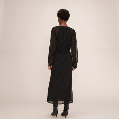 Vestido preto comprido de mulher visto de costas com padrão de bolinhas e botas pretas