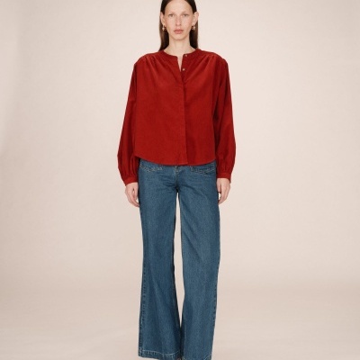 Mulher com top vermelho, calças de ganga largas azuis e sapatos castanhos.