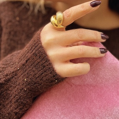 Mão com anel dourado e camisola castanha com lantejoulas sobre tecido rosa.