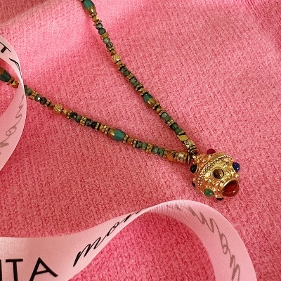 Colar colorido com conta dourada e pedras sobre tecido rosa e fita de cetim