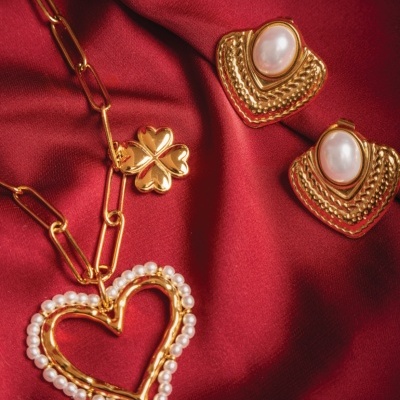 Colar com coração e trevo dourado e brincos dourados com pedra branca sobre tecido vermelho