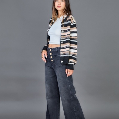 Mulher a usar camisola de riscas, top branco, calças de ganga largas e sapatos de salto preto em fundo cinzento