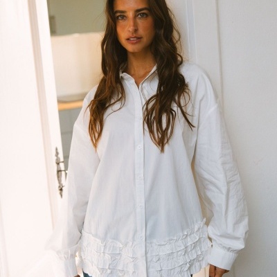 Blusa branca com folhos na parte inferior e jeans azuis em ambiente interior