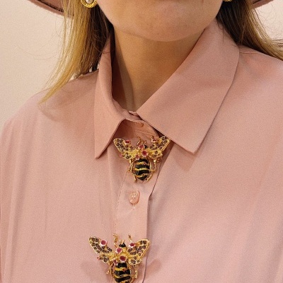 Blusa rosa com broches de abelha dourados, brincos dourados com pérola e chapéu rosa