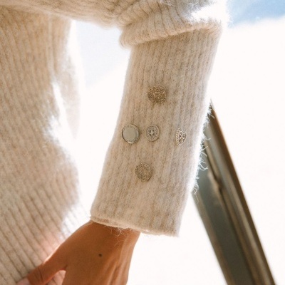 Manga de camisola bege com botões metálicos decorativos perto de uma janela