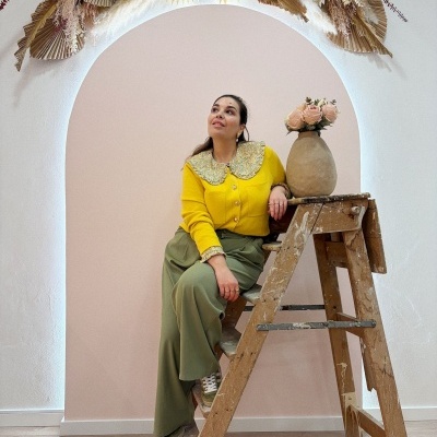 Mulher sentada numa escada de madeira com camisola amarela e calças verde-oliva