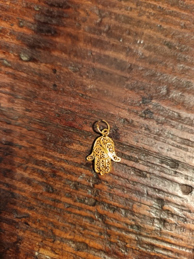 Pendente dourado em forma de mão sobre madeira rústica