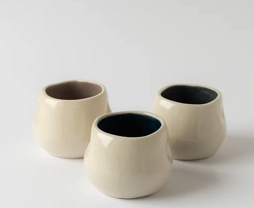 COPO COLORS BOLA MANU SOUZA Três vasos de cerâmica creme com interiores coloridos em superfície branca