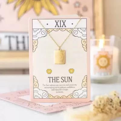Colar dourado com pendente do sol exibido em cartão decorativo com texto THE SUN.