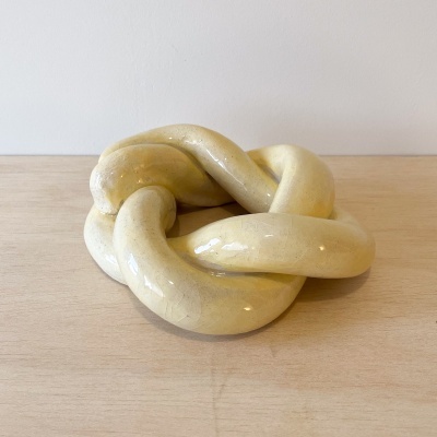 Escultura cerâmica amarelo claro com acabamento brilhante sobre mesa de madeira