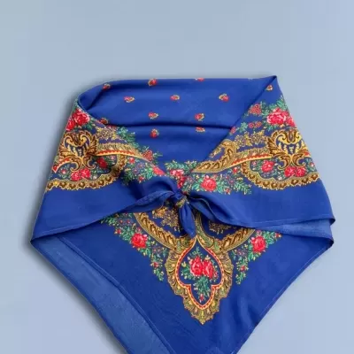 Lenço azul com padrão floral vermelho, verde e dourado, tecido suave e nó no centro
