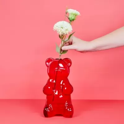 Vaso de vidro vermelho em forma de urso e flor branca num fundo rosa