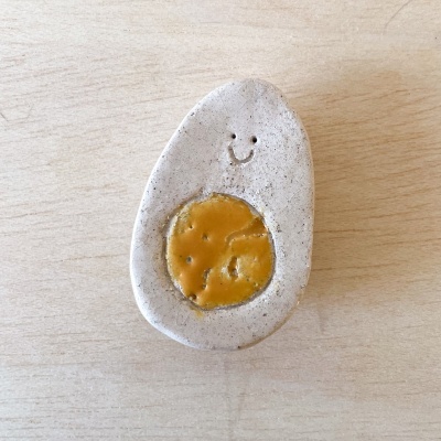 Objeto cerâmico em forma de ovo com rosto sorridente e centro amarelo.