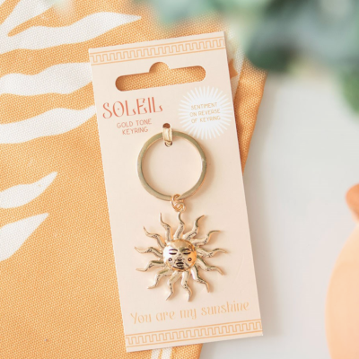 Chaveiro dourado em forma de sol com rosto e texto no cartão
