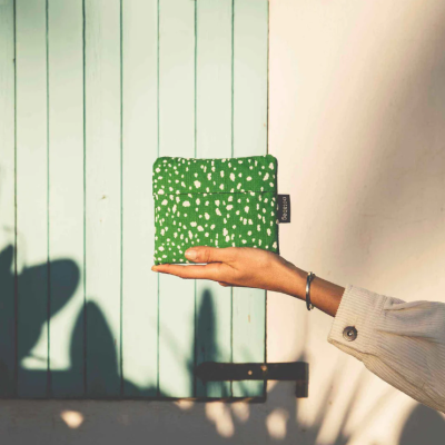 Bolsa verde com manchas brancas segurada junto a uma porta azul claro