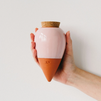Recipiente de cerâmica rosa e terracota com tampa de cortiça na mão
