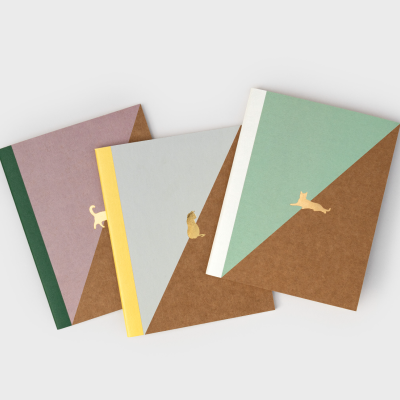 Três cadernos com capas coloridas e desenhos dourados de gatos.