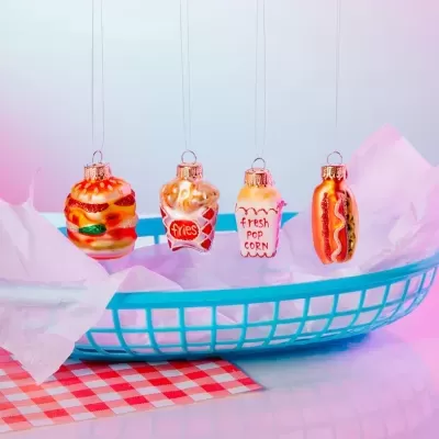 Ornamentos natalícios em forma de comida rápida pendurados sobre uma cesta azul com toalha xadrez