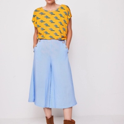 Mulher com t-shirt amarela com padrão azul, calças azuis largas e botas castanhas