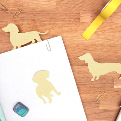 Autocolantes de cães, clips dourados, fita adesiva amarela e borracha azul sobre superfície de madeira