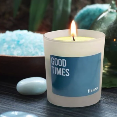 Vela acesa em copo branco com etiqueta azul GOOD TIMES