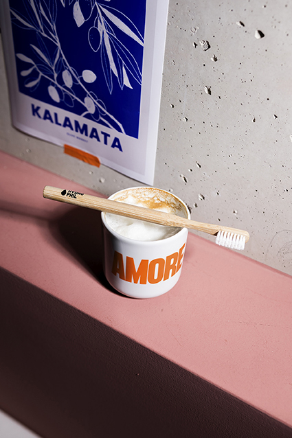 Escova de dentes de madeira sobre chávena com bebida e arte azul na parede.